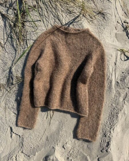 Brun Ivy Sweater fra PetiteKnit ligger i sandet.
