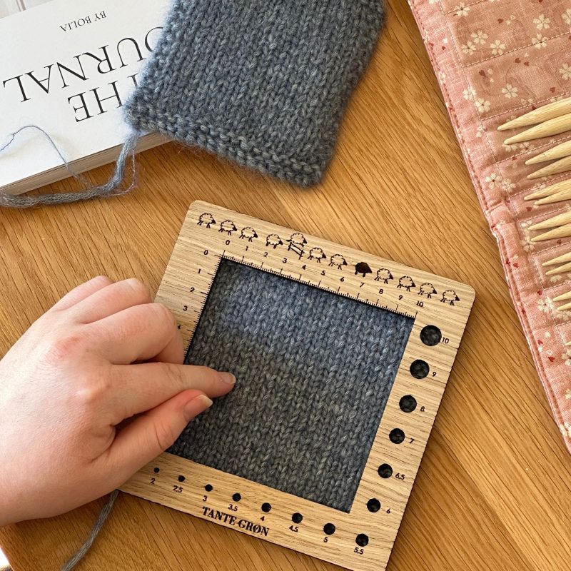 En person er ved at måle sin strikkefasthed på sin strikkeprøve, med sin strikkefasthedsmåler.